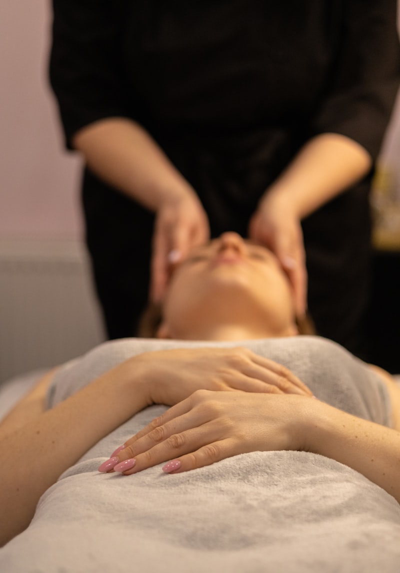 Woman lying face-up on a massage bed, eyes closed and peaceful, therapist gently cradling her head